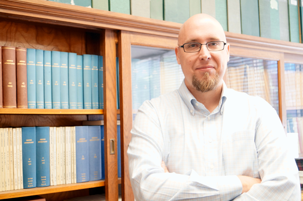 Ethan Watrall, standing in front of a bookcase